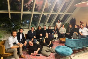 Gruppenfoto der Teilnehmer des Archicooking-Events in einer modernen Lounge mit Glasdecke im Smartvillage München. Die Gruppe sitzt und liegt entspannt auf stilvollen Designermöbeln, umgeben von Pflanzen.