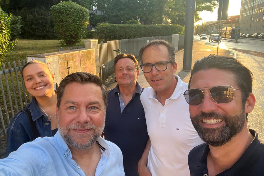Fünf Personen stehen bei Sonnenuntergang lachend zusammen auf dem Gehweg in München. Sie wirken entspannt und gut gelaunt nach einem gemeinsamen Besuch bei König + Neurath. Wenn du noch bestimmte Namen oder Rollen erwähnen möchtest (z. B. „Team von Hauser Office Design“), kann ich den Text entsprechend anpassen.