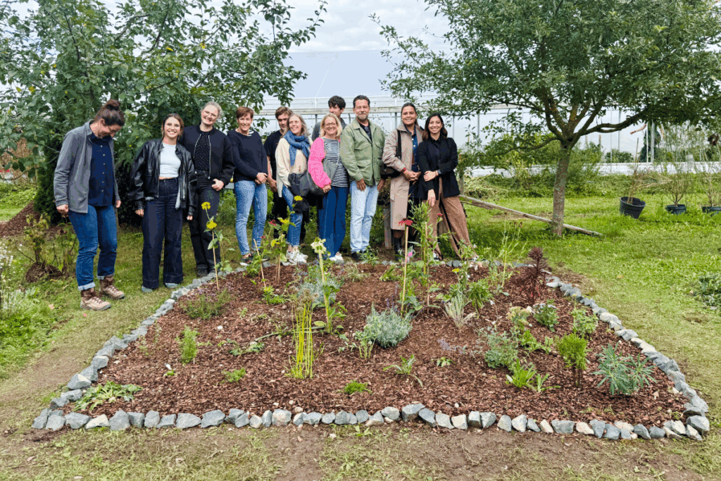 Gruppenfoto von rund einem Dutzend Personen, die lächelnd um ein neu bepflanztes, mit Steinen eingefasstes Blumenbeet im Garten stehen.