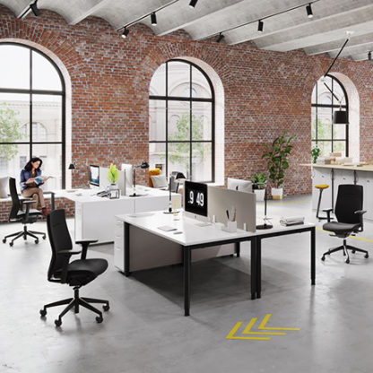 Moderne Büroarbeitsplätze von König + Neurath mit ergonomischen Stühlen und großzügigen Schreibtischen in einem Loft-Büro mit Ziegelmauern und großen Fenstern, belebt durch Tageslicht.