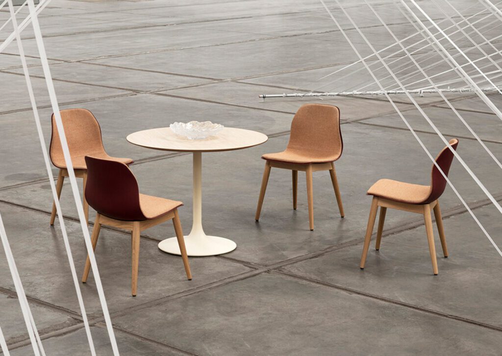 Ein kleiner runder Tisch in weiß und 4 Stuhle mit Holzgestell und Polsterung in hellen Farben auf einem dunkelgrauen Boden.