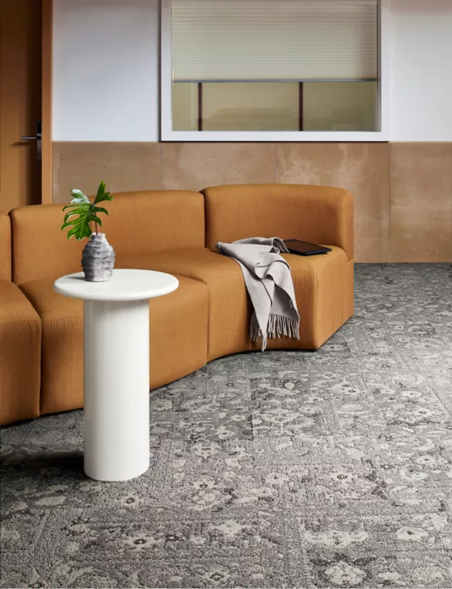 Ein grauer Teppich von Interface mit verschiedenen Blumenmustern schmückt den Raum. Ein Ledersessel in Schalengrün und ein weißer Beistelltisch vervollständigen die Einrichtung.