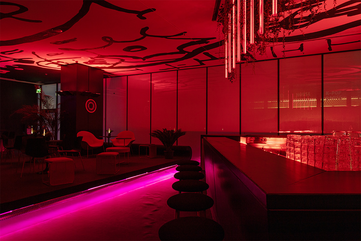 Stimmungsvolle Bar im Live/Evil Jazz-Club, beleuchtet in dramatischem Rot, mit modernen Sitzgelegenheiten und einer markanten Deckengestaltung, die eine einladende Atmosphäre für Musikliebhaber im Herzen Münchens schafft.