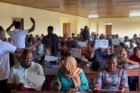 Teilnehmer in einem Klassenzimmer in Tansania halten stolz ihre Imsinne Whiteboards hoch, auf denen verschiedene Konzepte und Ideen skizziert sind, während eine lebhafte Diskussion im Gange ist, was die globale Reichweite und den Bildungseinfluss von Imsinne Produkten zeigt.