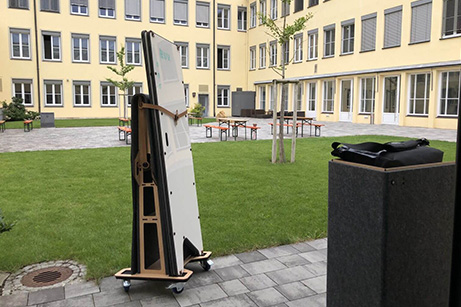 Ein Imsinne mobiles Whiteboard steht auf einem grünen Innenhof eines modernen Bildungszentrums, bereit für eine Outdoor-Lernsession, was die Mobilität und Anpassungsfähigkeit der Imsinne Bildungsprodukte an unterschiedliche Lernumgebungen illustriert.