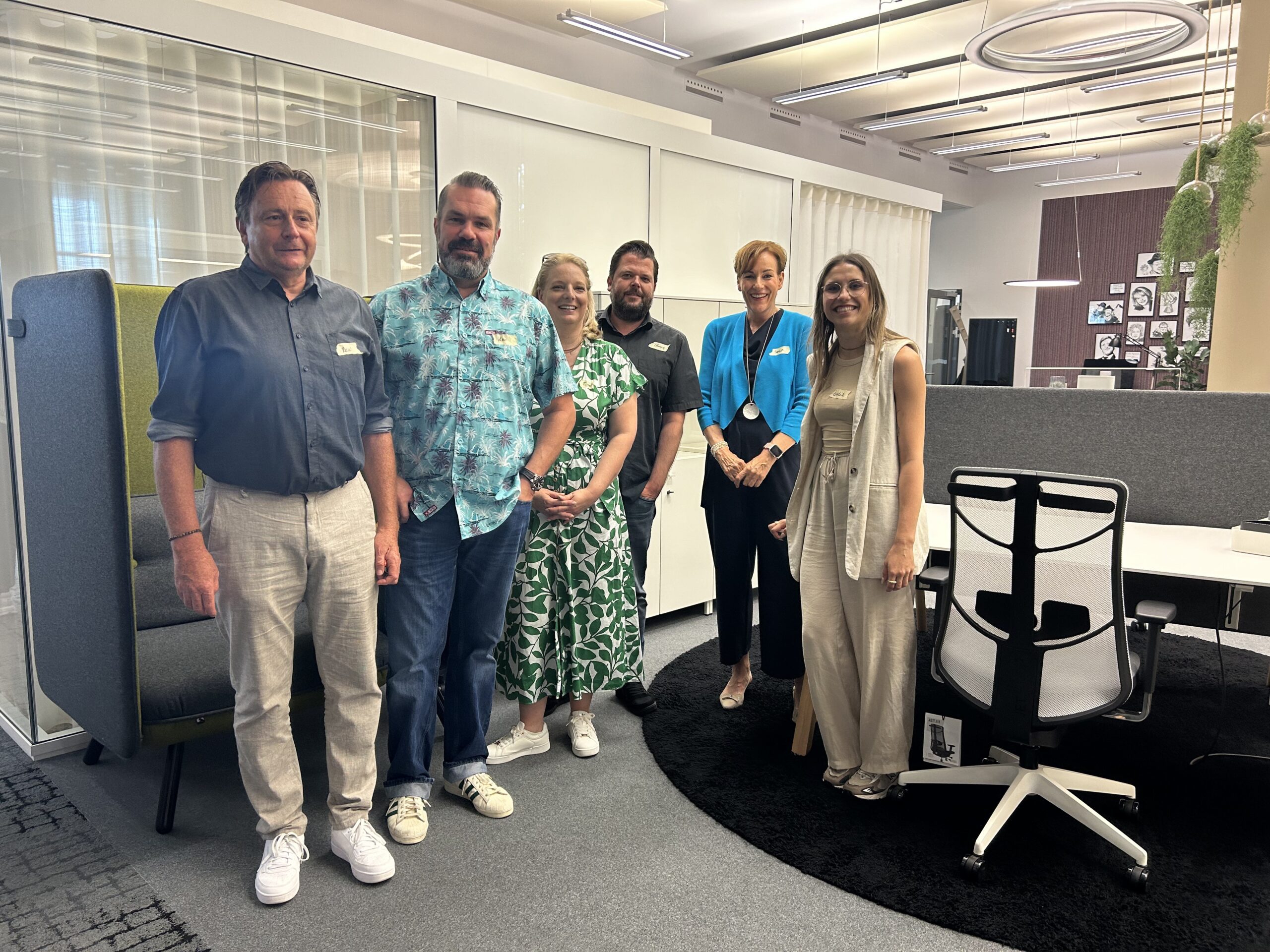 Gruppenbild beim K+N Barcamp: Sechs Teilnehmende stehen lächelnd in einem modernen Büro mit stylischem Mobiliar, darunter ergonomische Bürostühle und Akustikmöbel. Die entspannte Atmosphäre spiegelt das kreative und kollegiale Umfeld des Events wider.