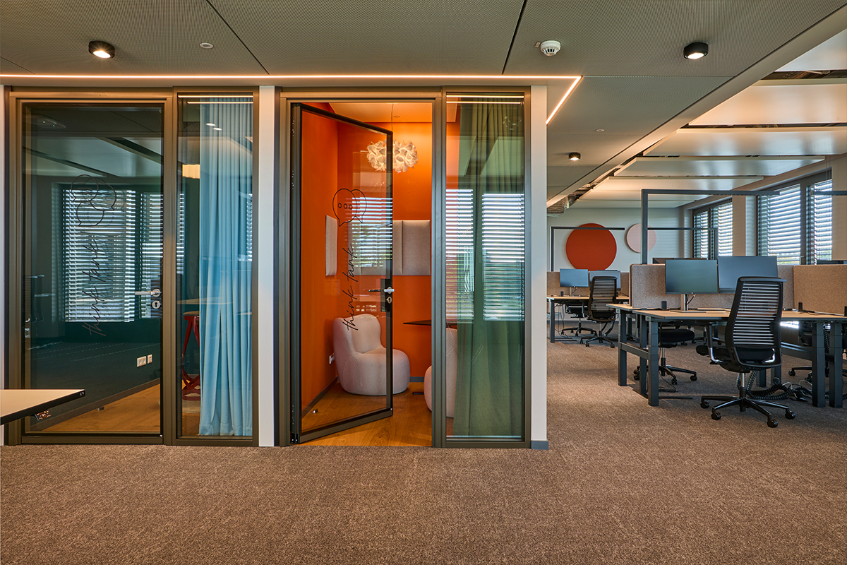Eine moderne Arbeitsumgebung mit Glastrennwänden und einer Telefonkabine in warmen Orange-Tönen, Teil der Bürogestaltung für BNP Paribas in München