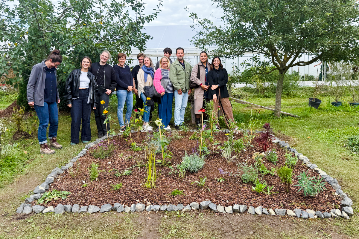 Gruppenfoto von rund einem Dutzend Personen, die lächelnd um ein neu bepflanztes, mit Steinen eingefasstes Blumenbeet im Garten stehen.